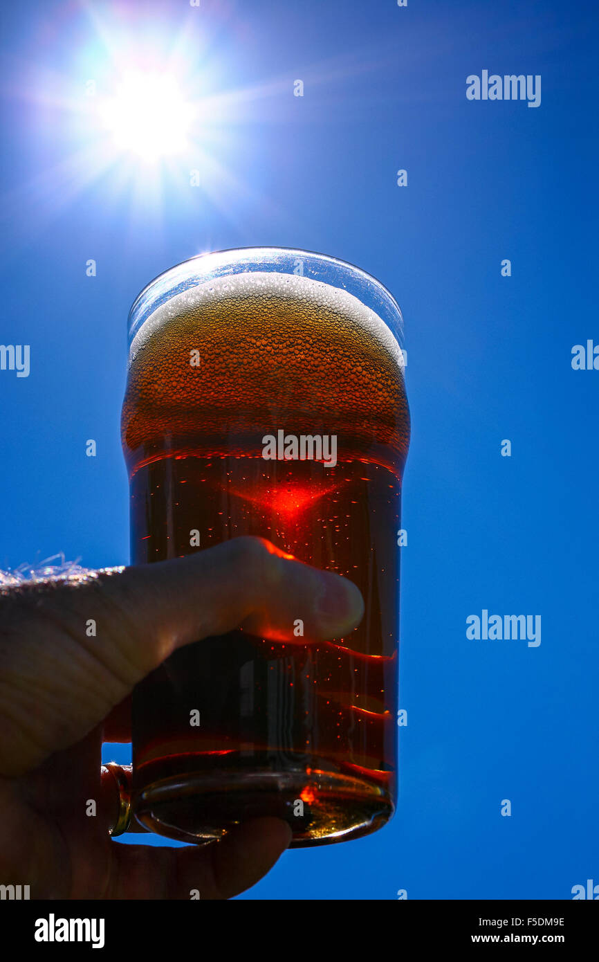 Man mano che tiene una pinta bicchiere di birra amara contro un Cielo di estate blu Foto Stock