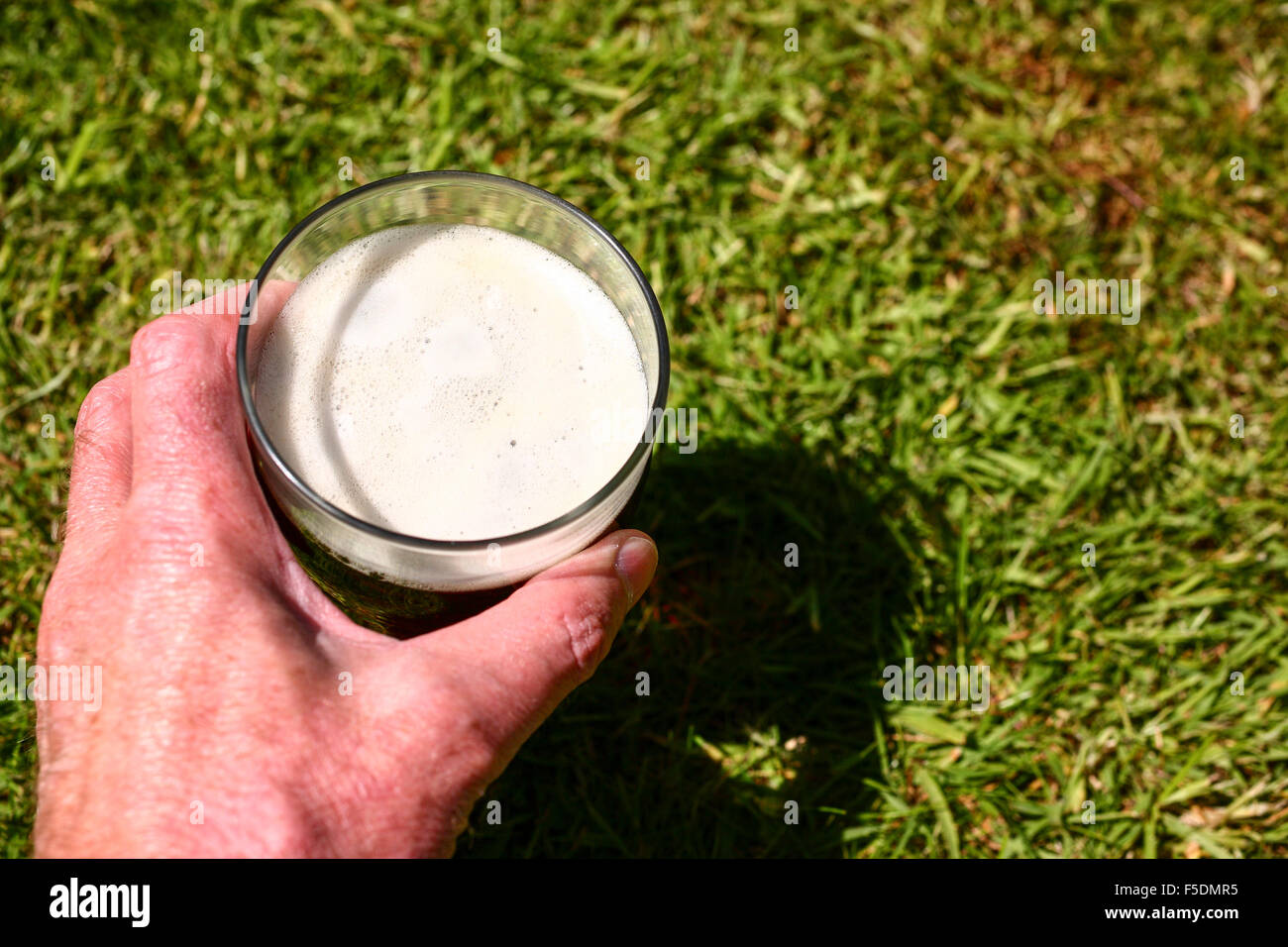 Man mano che tiene una pinta bicchiere di birra amaro al di fuori in estate Foto Stock