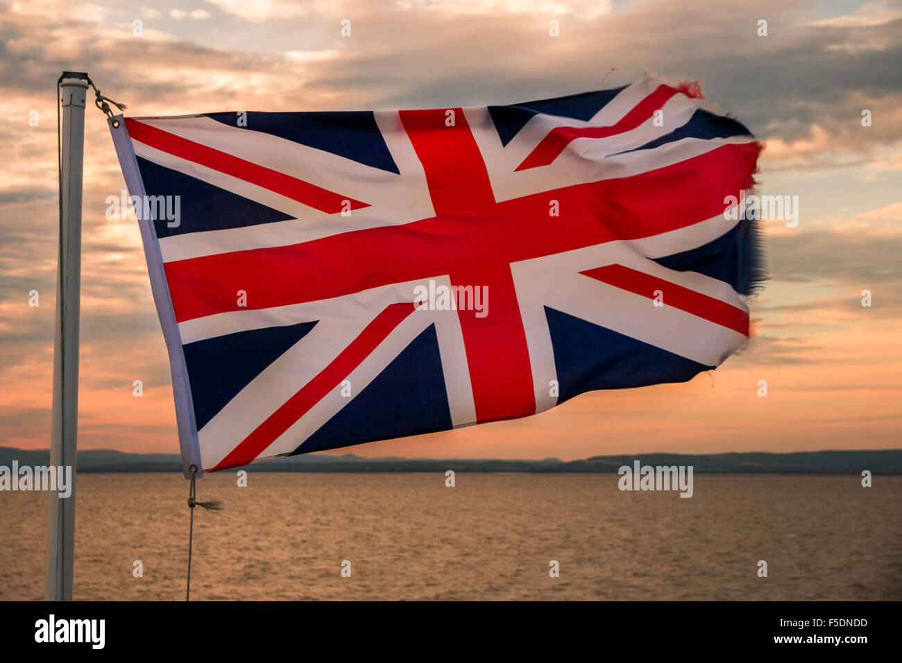 Una Unione Jack battenti contro un tramonto sul mare Foto Stock