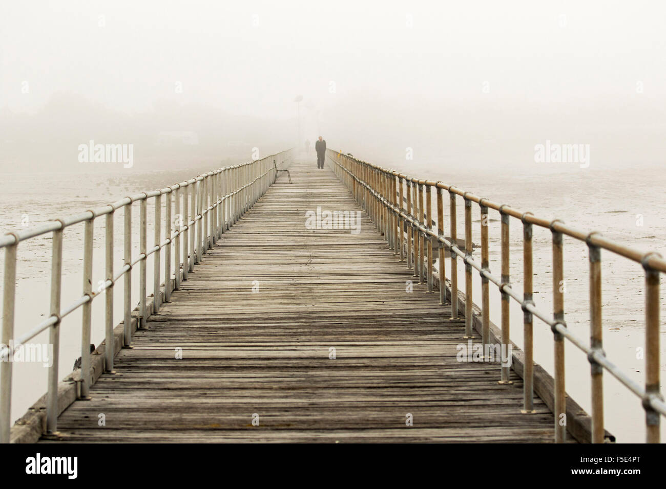 Uomo che cammina su una lunga storico pontile in legno a Port Germein che spears fuori di oceano invisibile & svanisce nella fitta nebbia di mattina Foto Stock