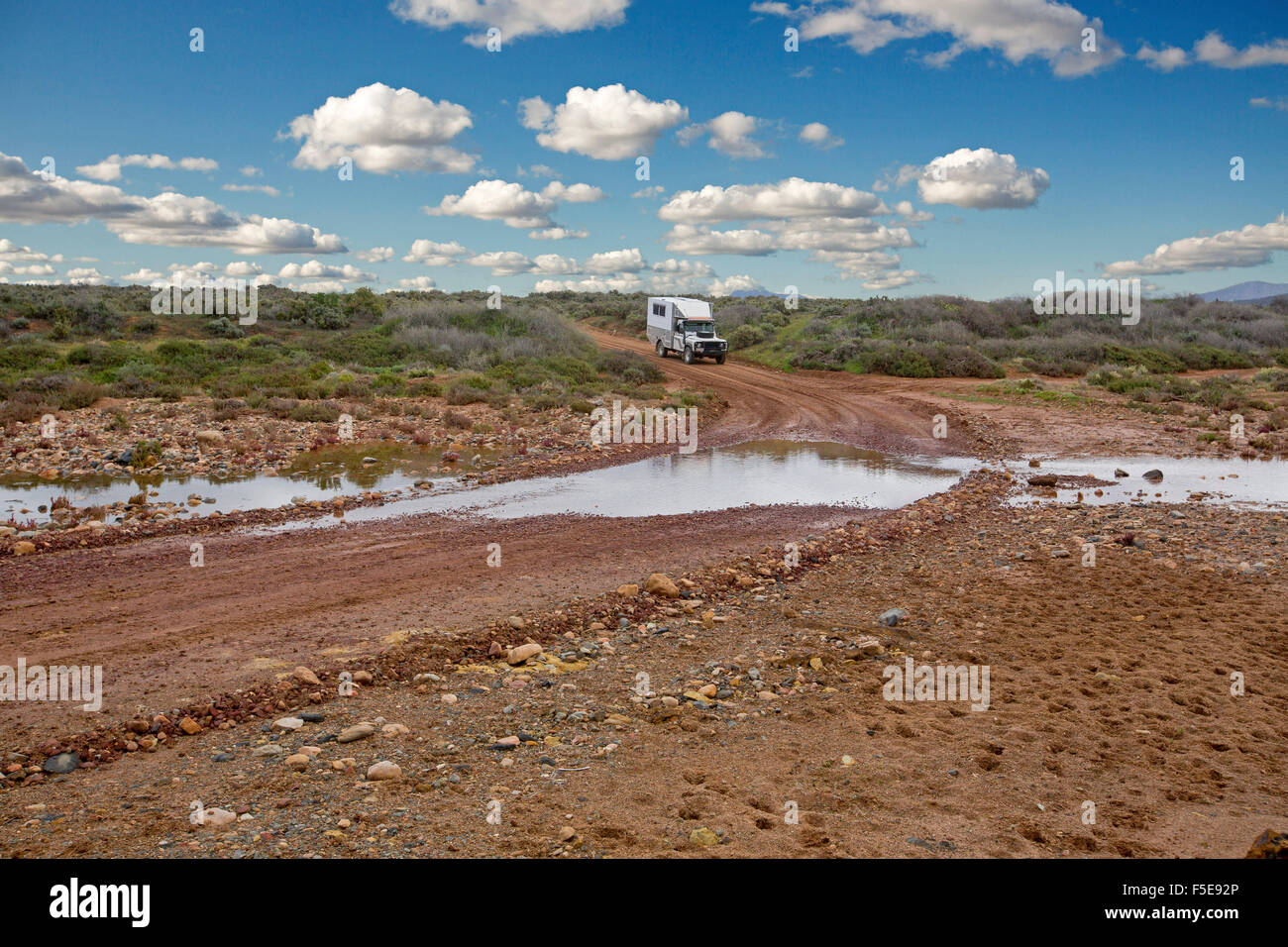 La trazione a quattro ruote motrici CAMPER / MOTORHOME circa a guidare attraverso acqua a creek incrocio su Australian Outback road orlate da una bassa vegetazione dopo la pioggia Foto Stock