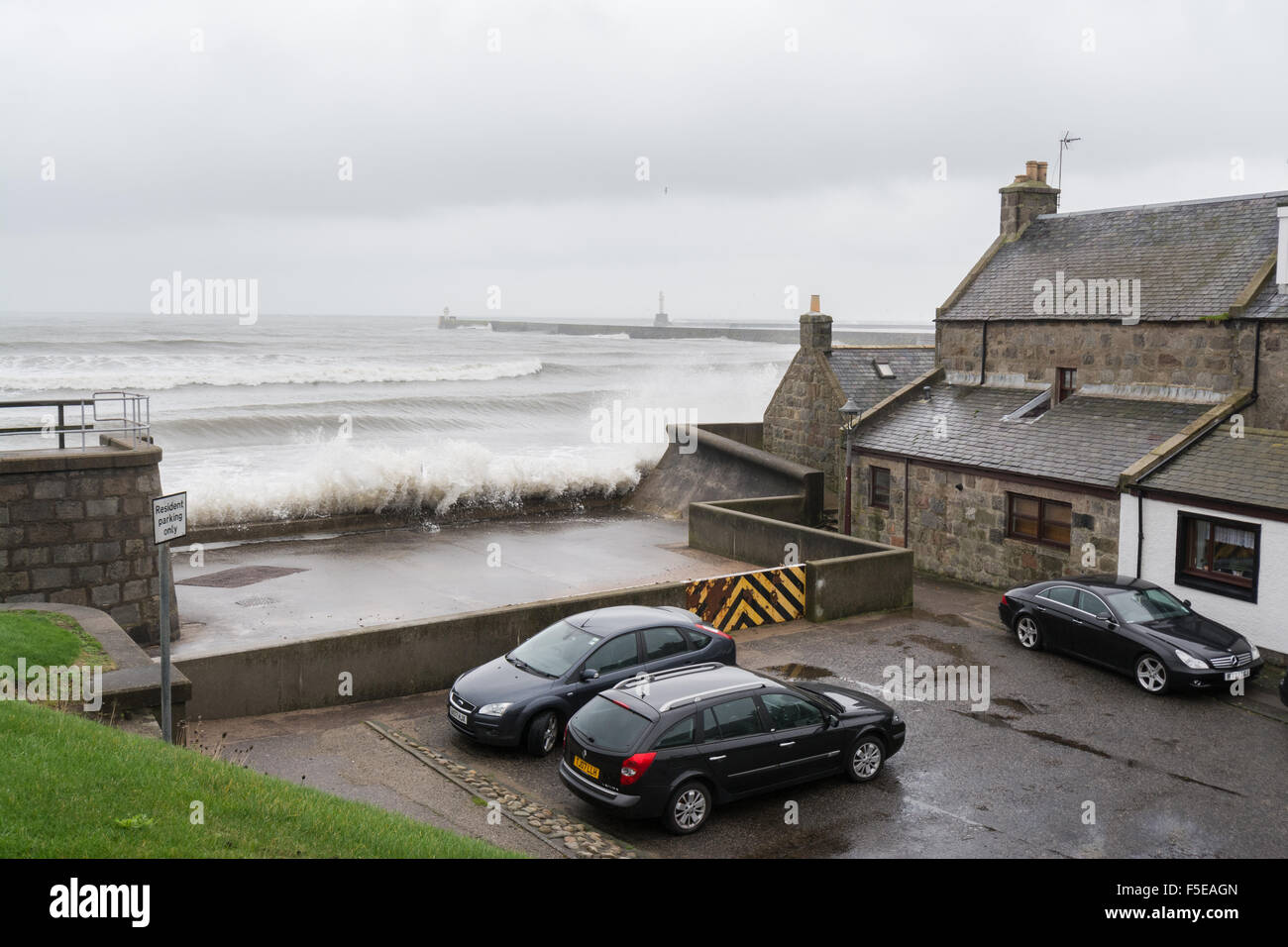 Onde che si schiantano contro le difese del mare nella parte anteriore del granito vecchie case di pescatori e automobili, Footdee, Aberdeen Scotland, Regno Unito Foto Stock