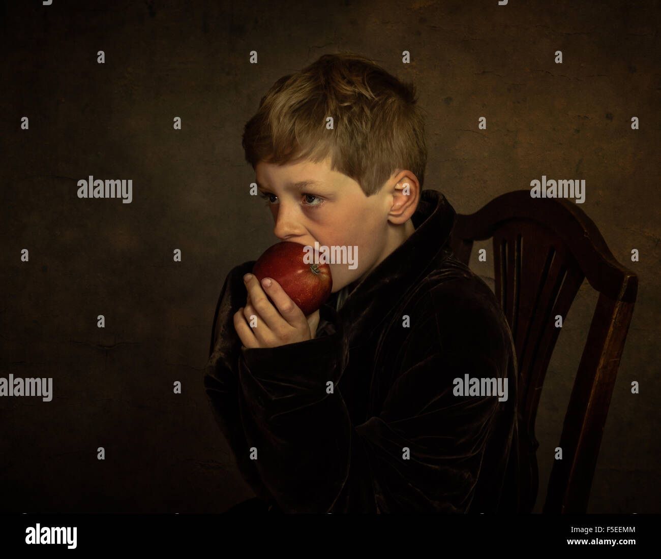 Bella arte ritratto di un ragazzo seduto su una sedia mangiare una mela Foto Stock