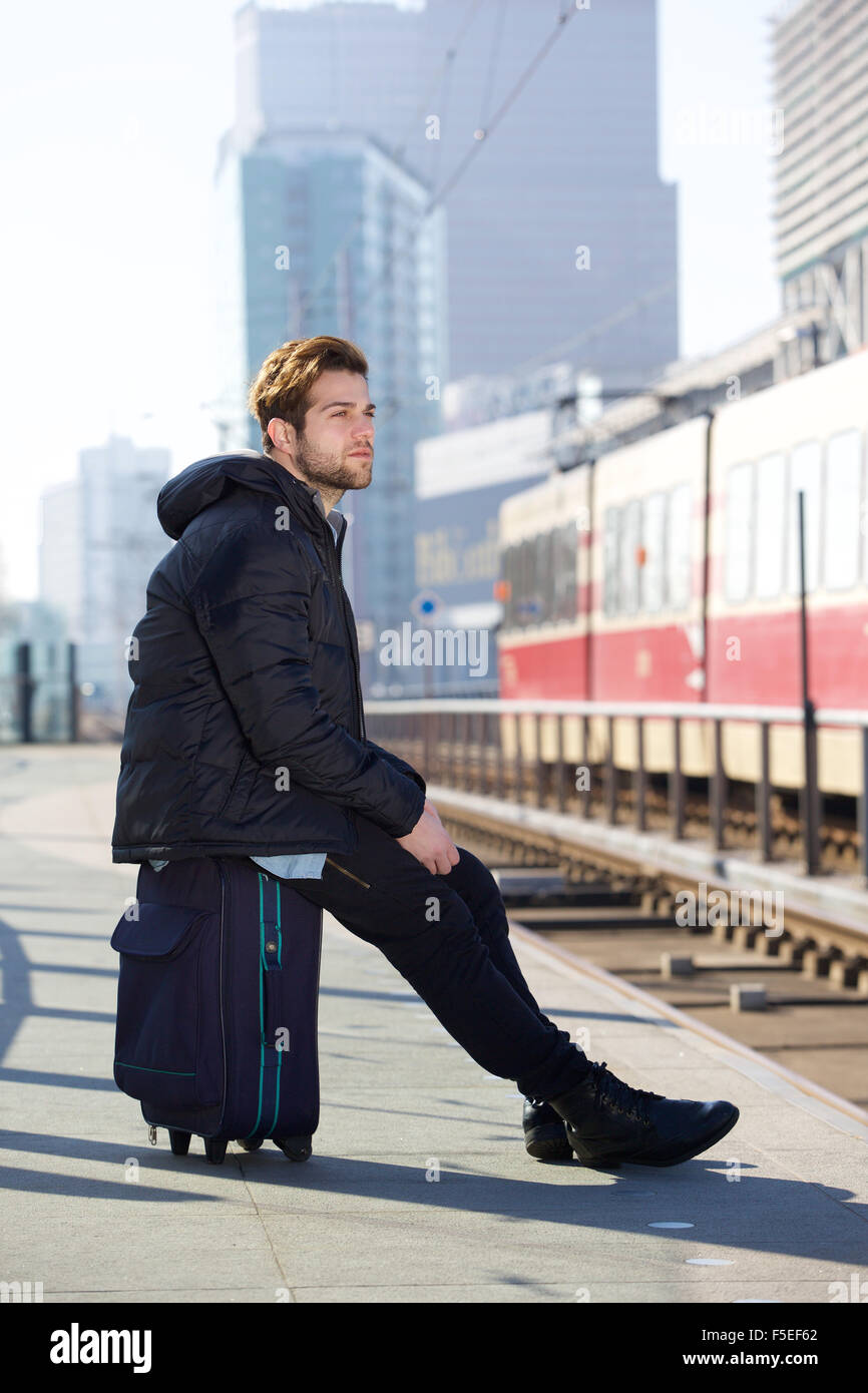 Ritratto di un giovane attraente uomo seduto e in attesa di un treno alla stazione Foto Stock