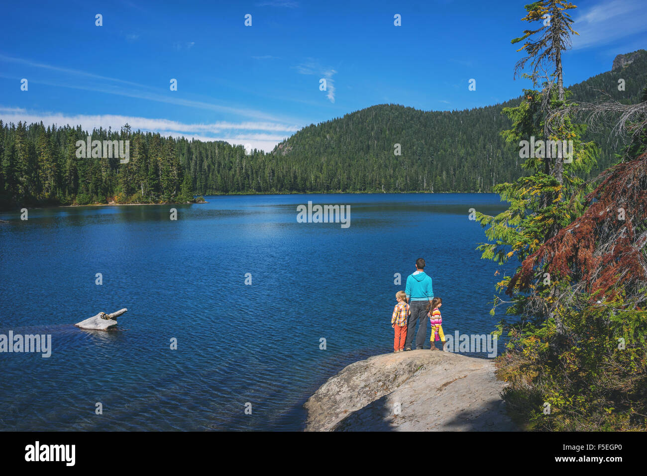 Uomo con due bambini in piedi su una roccia dal lago Foto Stock