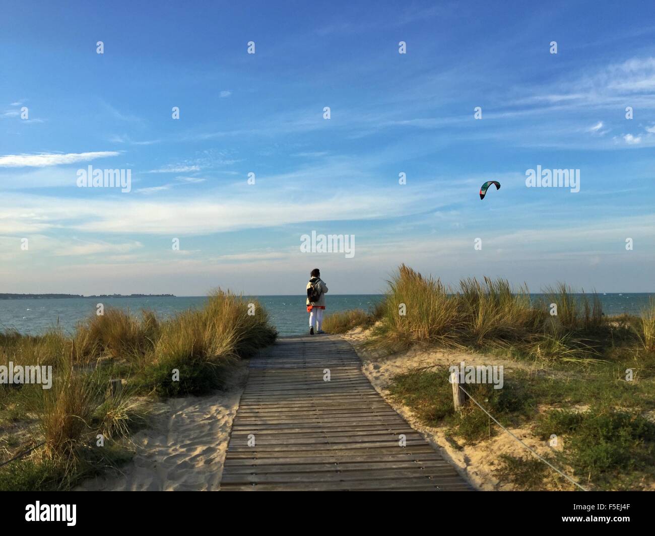 Vista posteriore di una donna in piedi sulla spiaggia guardando kiteboarder, La Rochelle, Francia Foto Stock