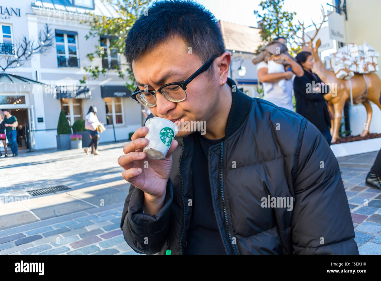 Parigi, Francia, uomo cinese a mangiare il gelato sulla strada di 'La Vallee Village " Shopping Centre, Starbucks Cafe Foto Stock