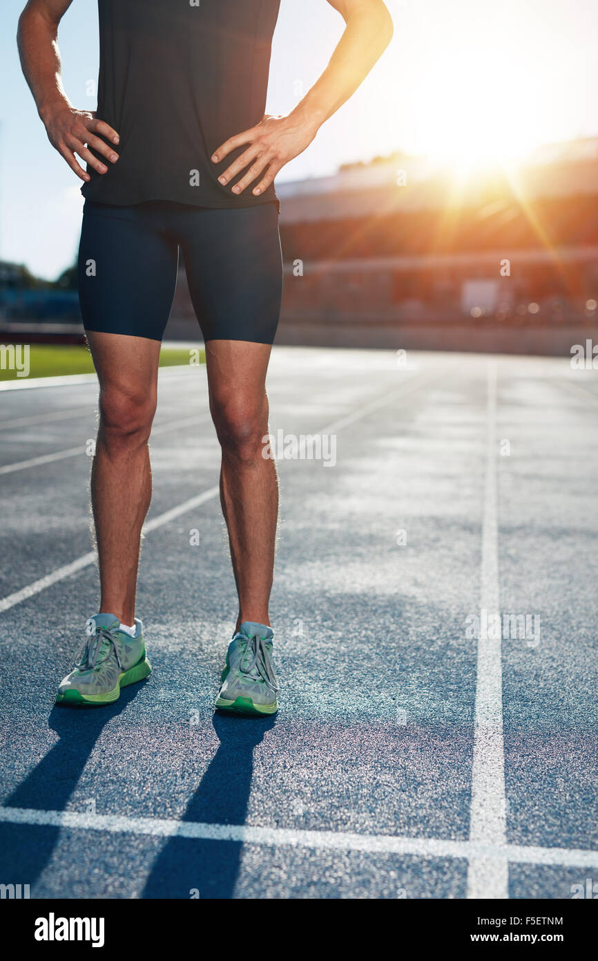 Sezione bassa colpo di atleta uomo in piedi sulla pista con le mani sui fianchi. Ritagliato shot dei maschi di runner su atletica in esecuzione Foto Stock