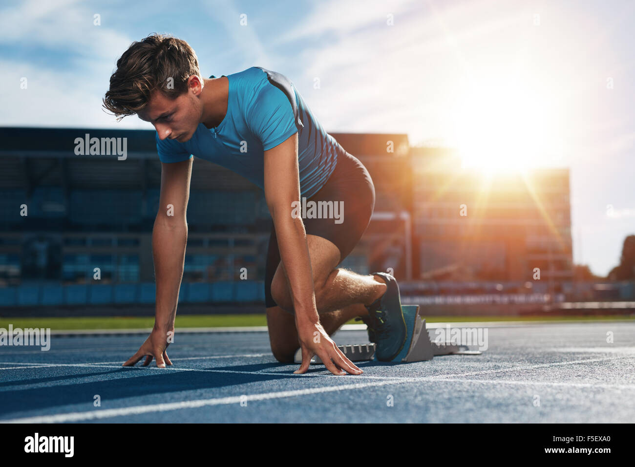 Giovane atleta maschio nel blocco di partenza sulla via di corsa. Giovane uomo nella posizione di partenza per la marcia su sport track. Sprinter abou Foto Stock