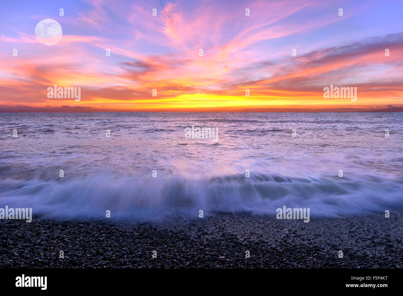 Ocean sunset luna è un colore pieno cielo con le onde che si infrangono sulla riva e il Full Moon Rising in background. Foto Stock