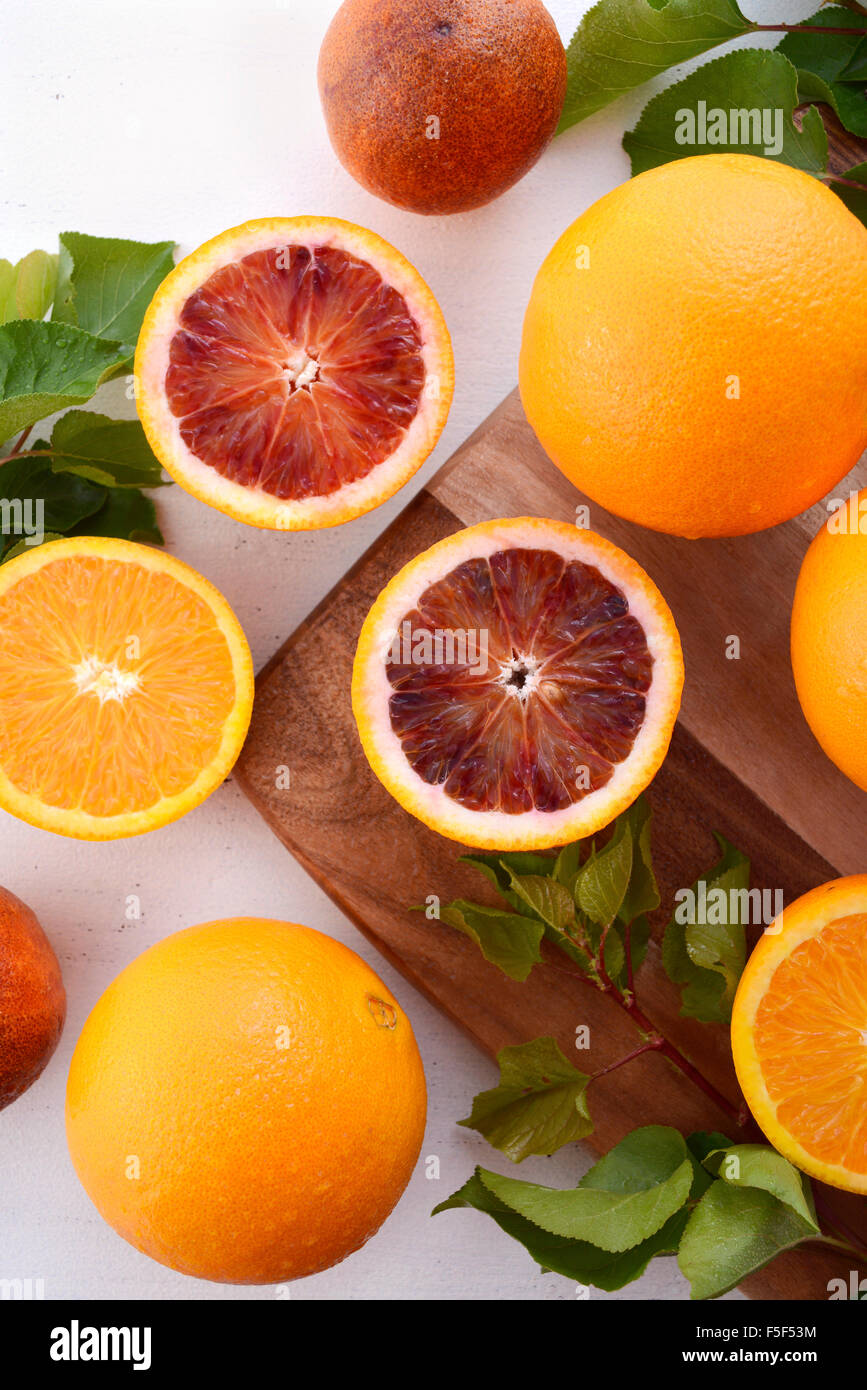 Misto di diverse varietà di ombelico e arance rosse sul tagliere con foglie sul bianco rustico tavolo in legno. Foto Stock