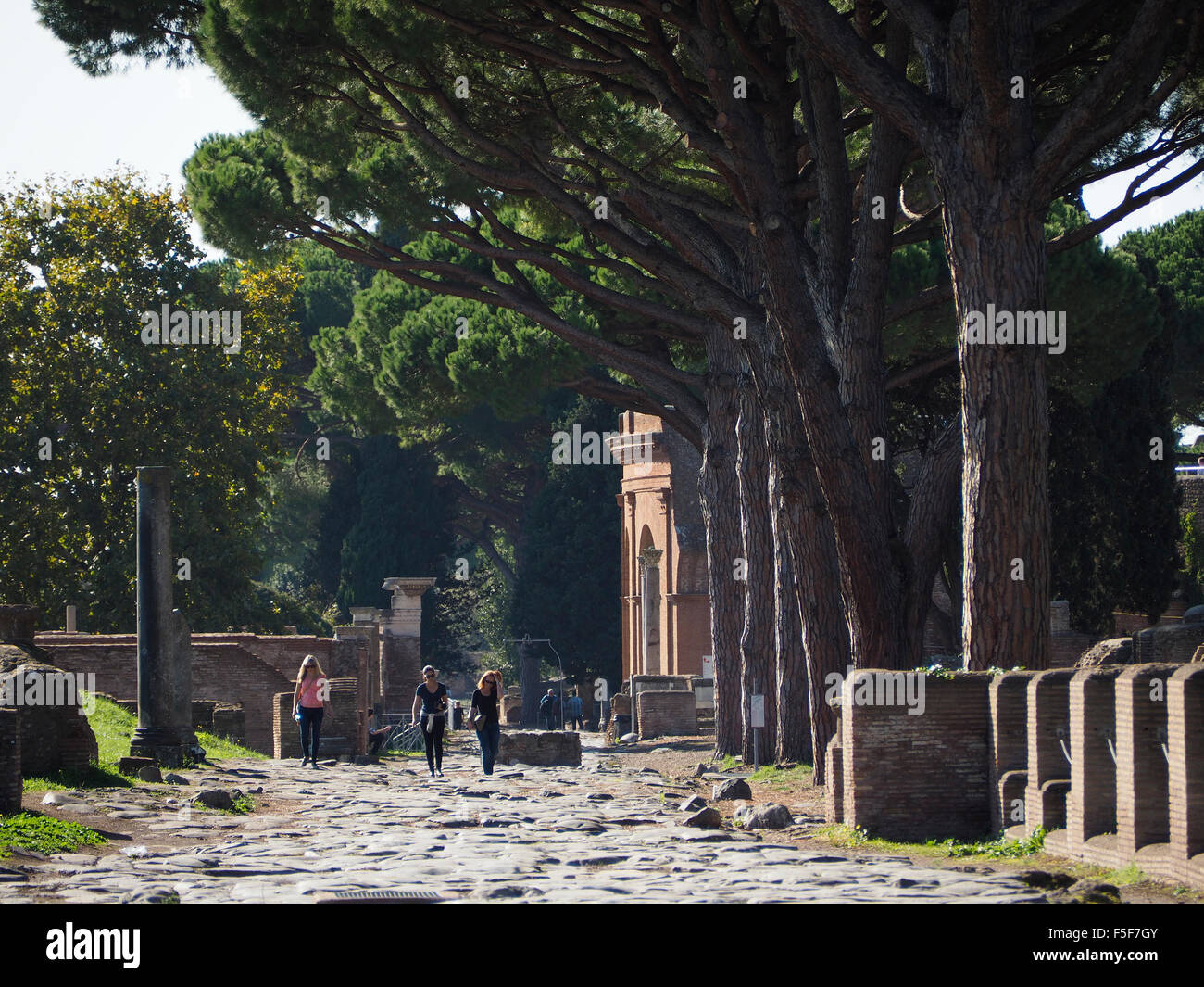 I turisti camminando sulla Osta Antica Via Decumana road, con l'ingresso al teatro visibile in background. Italia Foto Stock