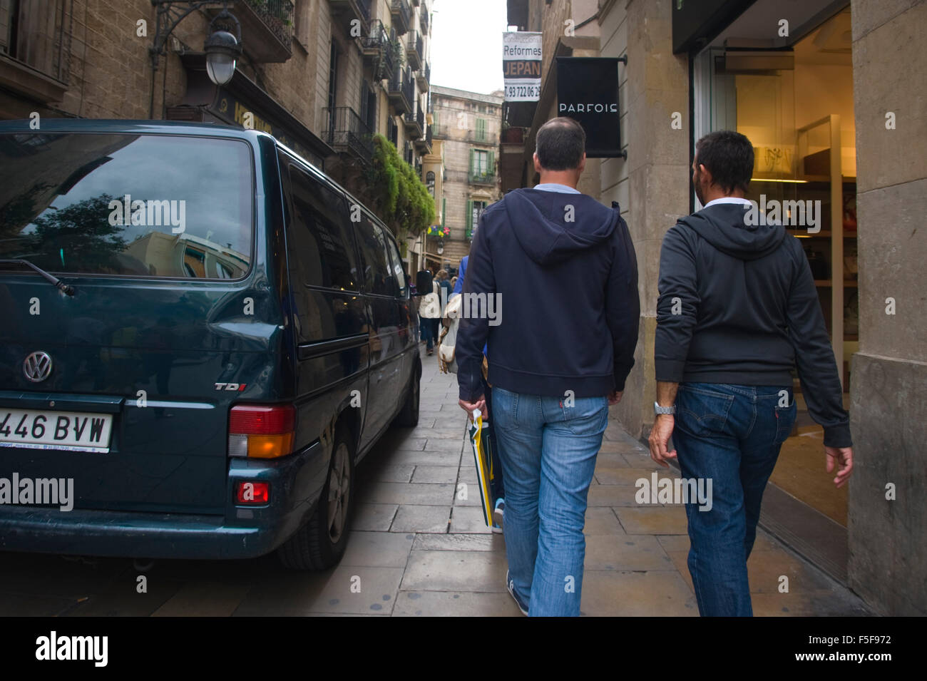 Due uomini che indossano jeans a piedi lungo la stretta strada dello shopping passato VW van a Barcellona Catalonia Spain ES Foto Stock