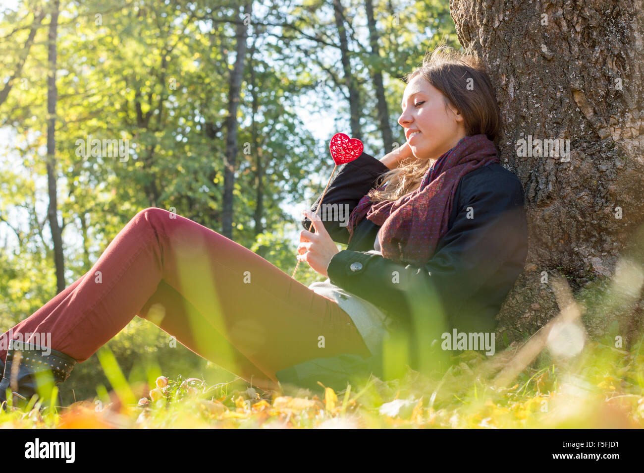 Bellissima ragazza con cuore rosso su un bastone mentre è seduto sull'erba. Relax in una giornata autunnale Foto Stock