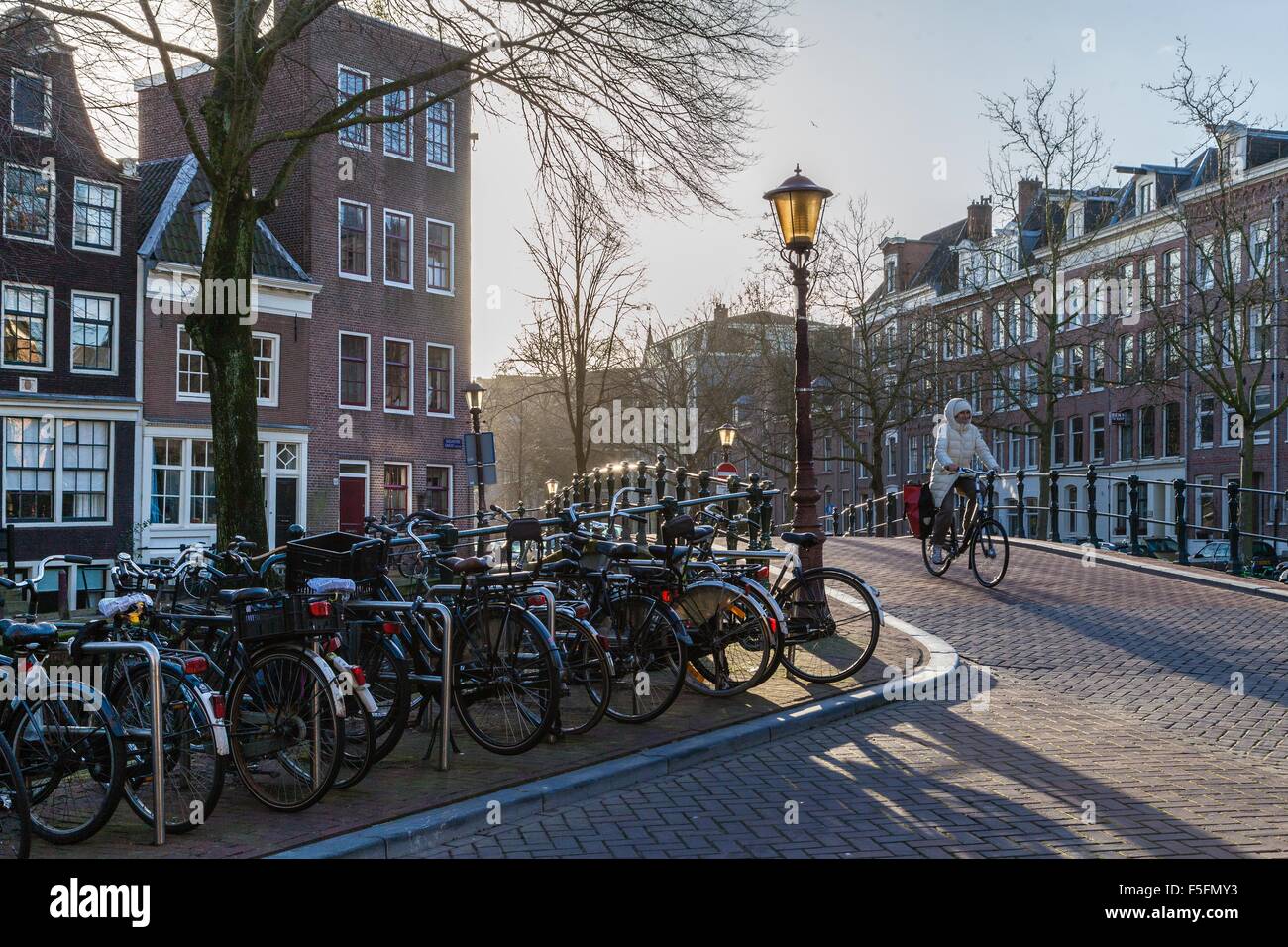 Escursioni in bicicletta lungo i canali di Amsterdam e oltre il ponte rivestiti con le biciclette e gli edifici storici in una fredda giornata invernale Foto Stock