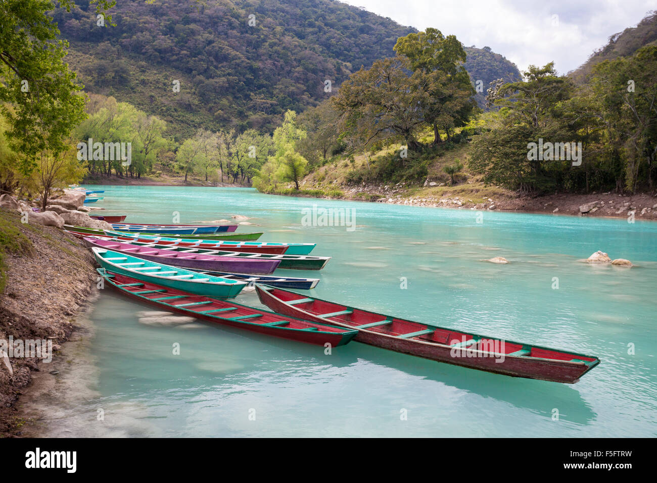 Canoe colorate fiancheggiano la riva dell'azzurro fiume Tampaon nella zona Huasteca Potosina di San Luis Potosi, Messico. Foto Stock