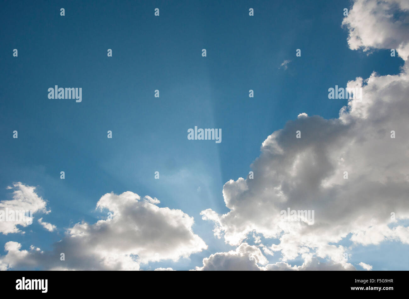 Scoppia la luce del sole attraverso le nuvole contro un cielo blu Foto Stock