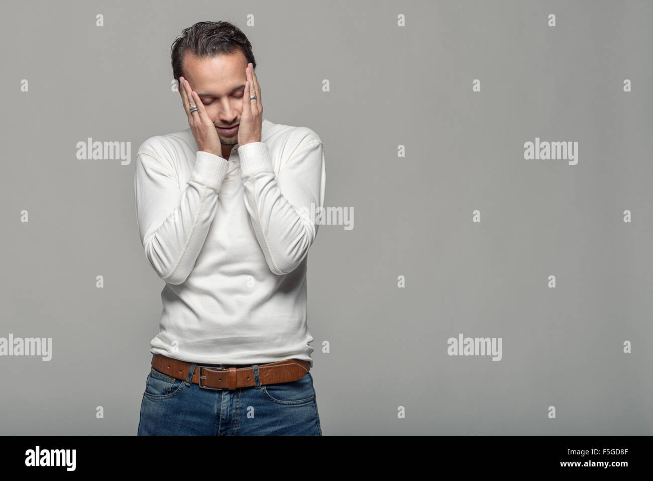 Mezzo Corpo colpo di una premurosa Giovane toccando il suo volto con gli occhi chiusi contro uno sfondo grigio con copia spazio. Foto Stock