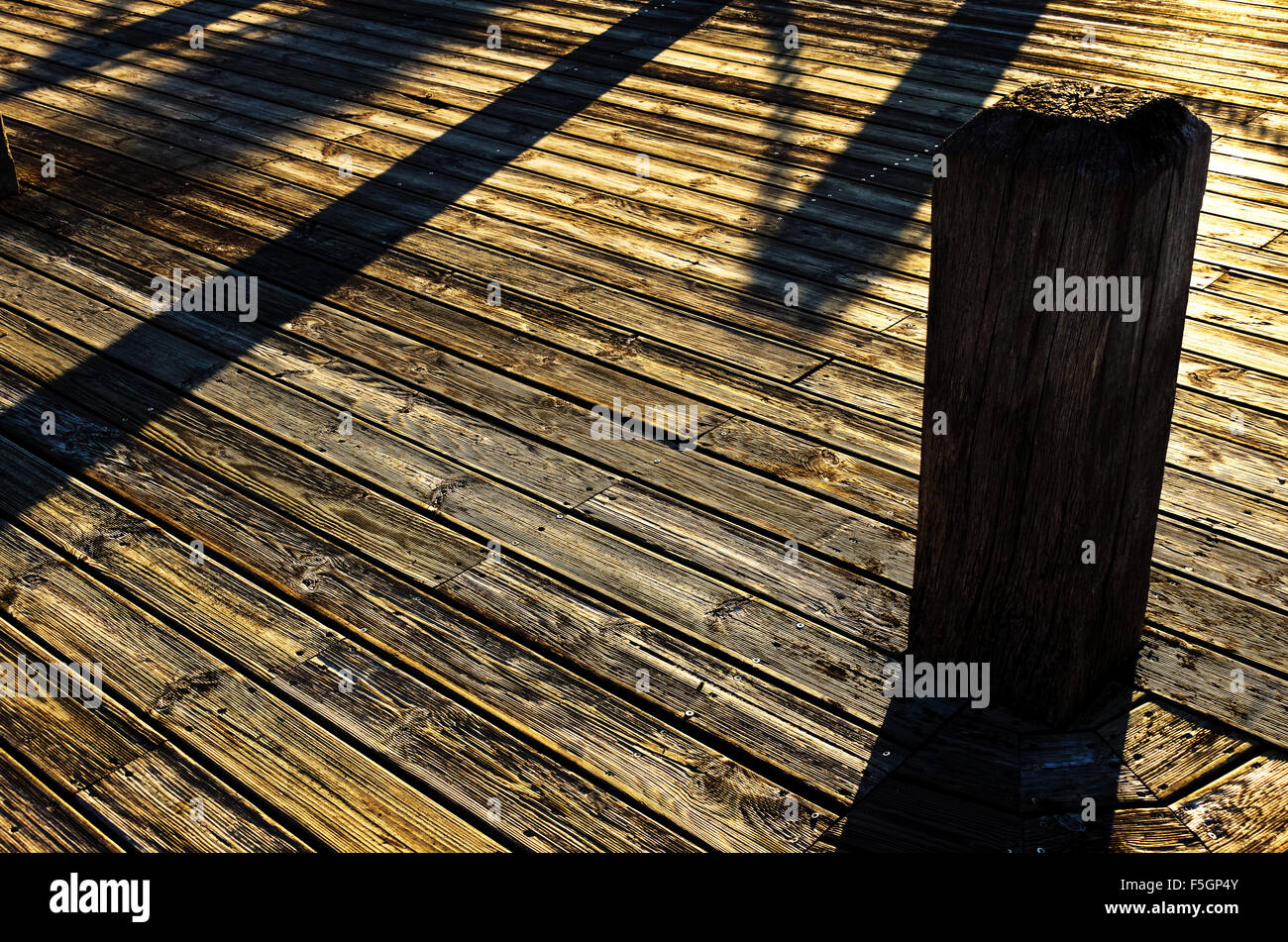 Decking in legno listellare riflesso dorato del sole al tramonto, forti ombre scure e bollard Foto Stock
