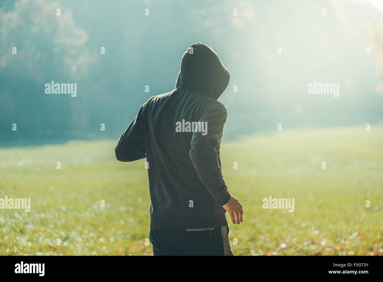 Uomo incappucciato jogging nel parco di inizio autunno mattina, sport e stile di vita sano concetto, dai toni rétro con immagine Foto Stock