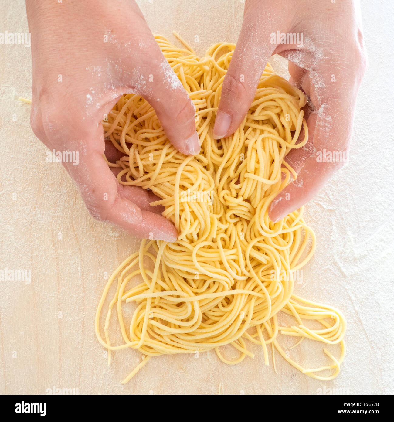 La donna le mani al lavoro per rendere home spaghetti fatti con farina e uova su una tavola di legno Foto Stock