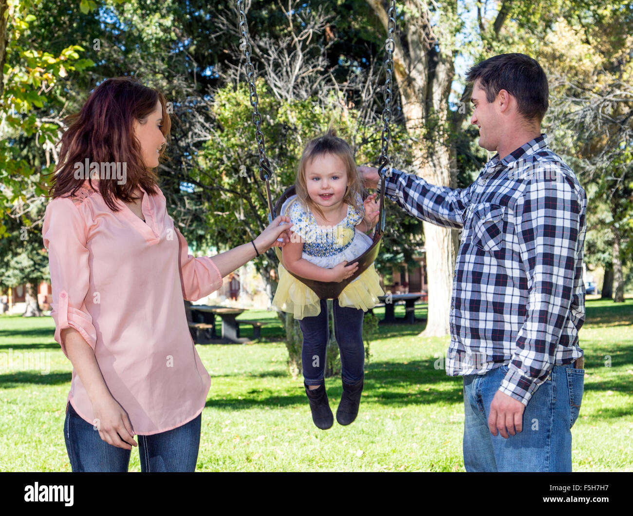 Padre, Madre e carino giovane figlia gioca su park altalene Foto Stock