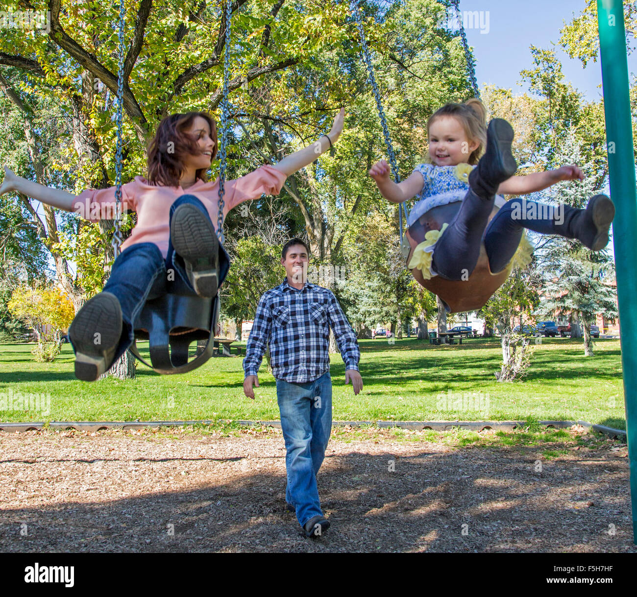 Padre, Madre e carino giovane figlia gioca su park altalene Foto Stock