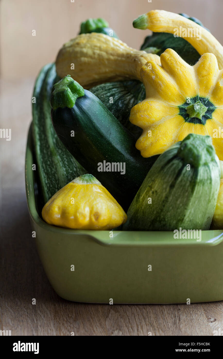 Un quadrato verde contenitore contiene una varietà di estate squash su una tavola di legno Foto Stock