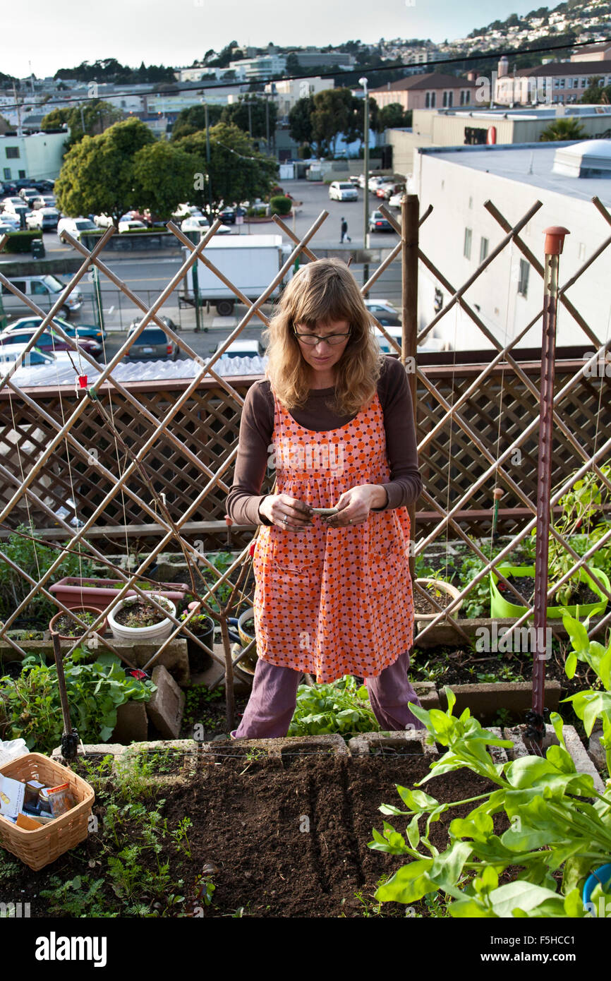 Una giovane donna in arancione funziona nel suo piccolo a terrazze giardino vegetale in San Francisco Foto Stock