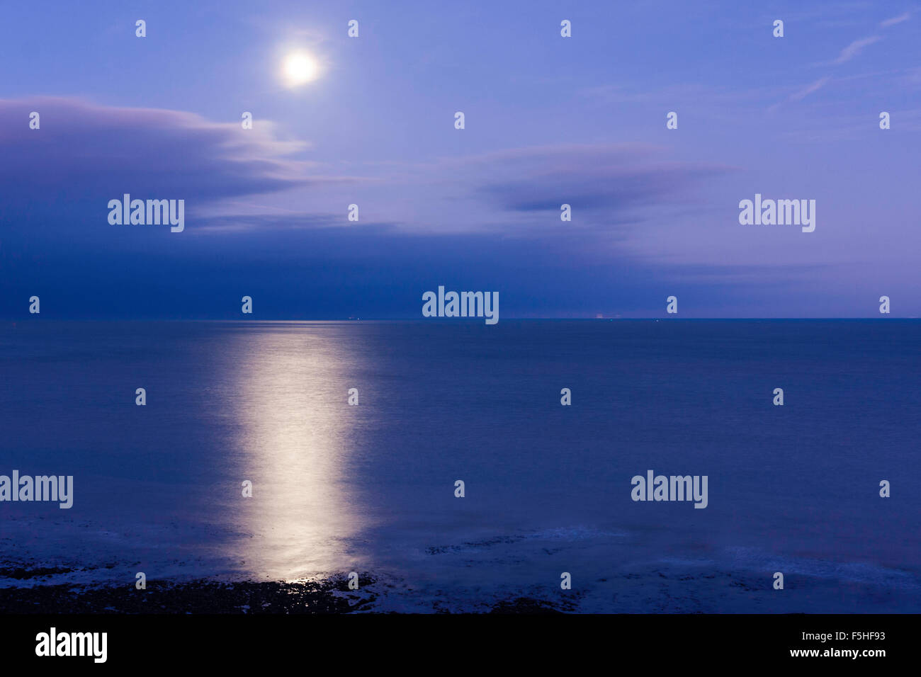 Super luna splendenti in un viola chiaro cielo blu sopra un mare di vongole, il canale della Manica, off alla costa del Kent a Ramsgate, con grande riflessione. Alcune nuvole. Foto Stock