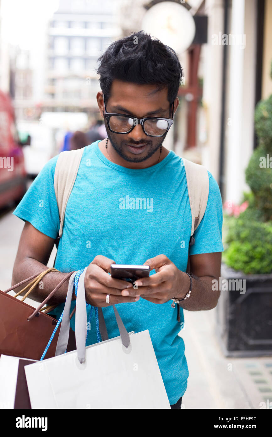 Giovane uomo indiano utilizzando il suo telefono e tenere borse per lo shopping Foto Stock