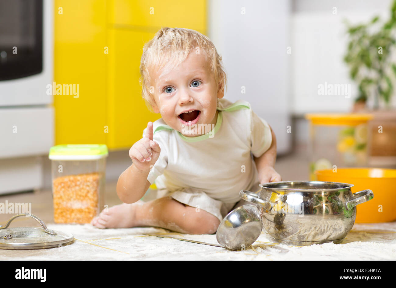 Giocoso bambino ragazzo con stoviglie e prodotti alimentari sul pavimento in cucina Foto Stock