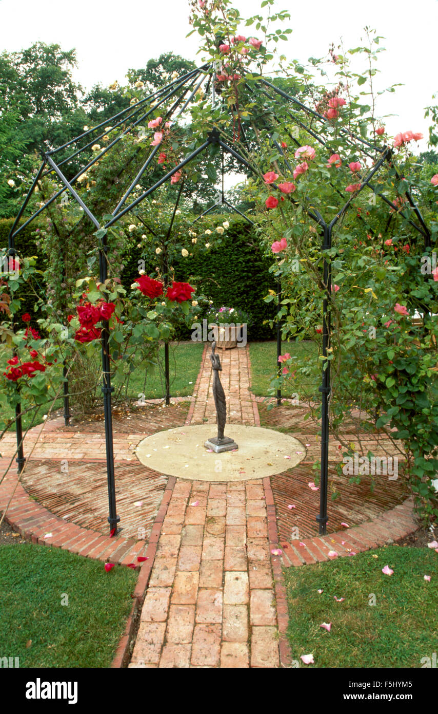 Mattone sentiero lastricato di pavimentazione circolare con rosa e rose rosse sul metallo nero gazebo Foto Stock