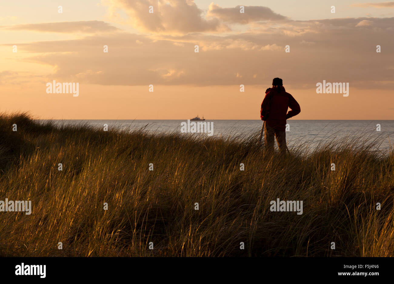 Un uomo con una telecamera su un treppiede che guarda al mare Foto Stock