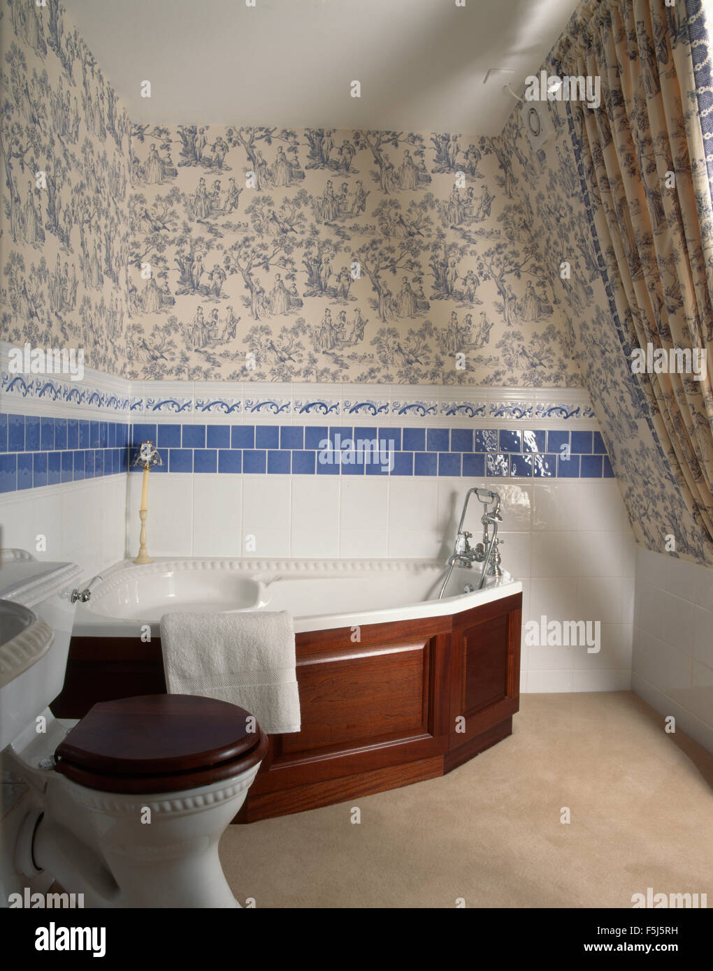 Toile de Jouy sfondo al di sopra di una vasca ad angolo con un pannello di mogano in un bagno degli anni novanta Foto Stock