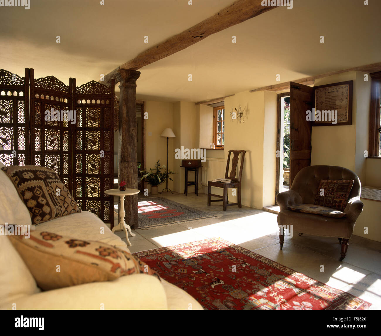 Indian traforature schermo in un cottage soleggiato soggiorno con una poltrona marrone e crema divano Foto Stock