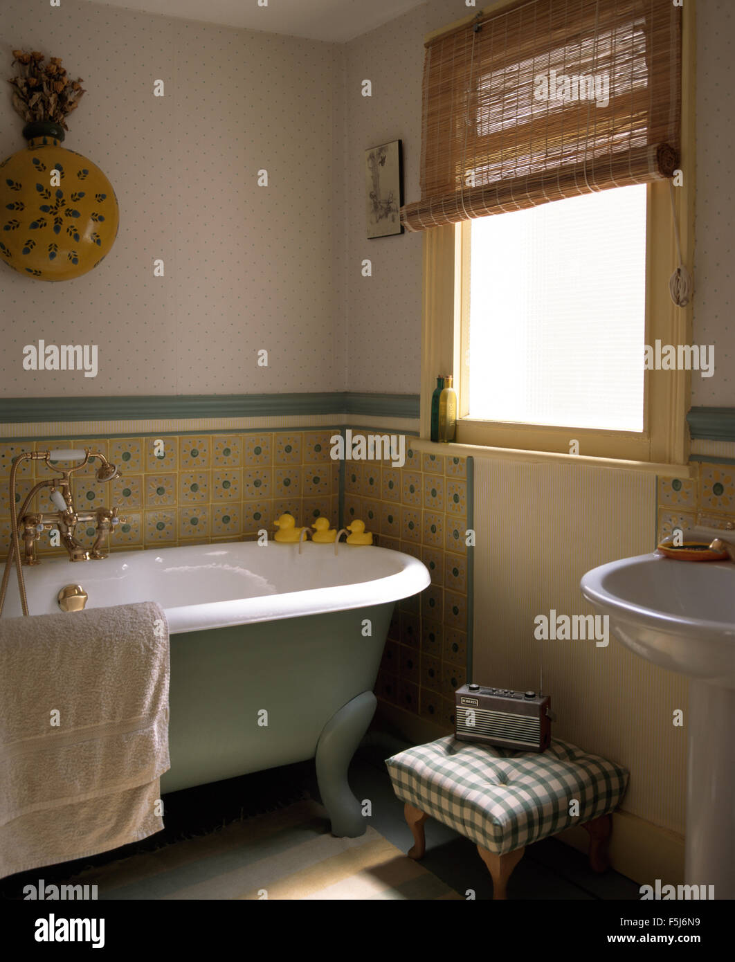 Piccolo Sgabello imbottito accanto a roll top bagno in un tradizionale bagno con pinoleum cieco sulla finestra Foto Stock