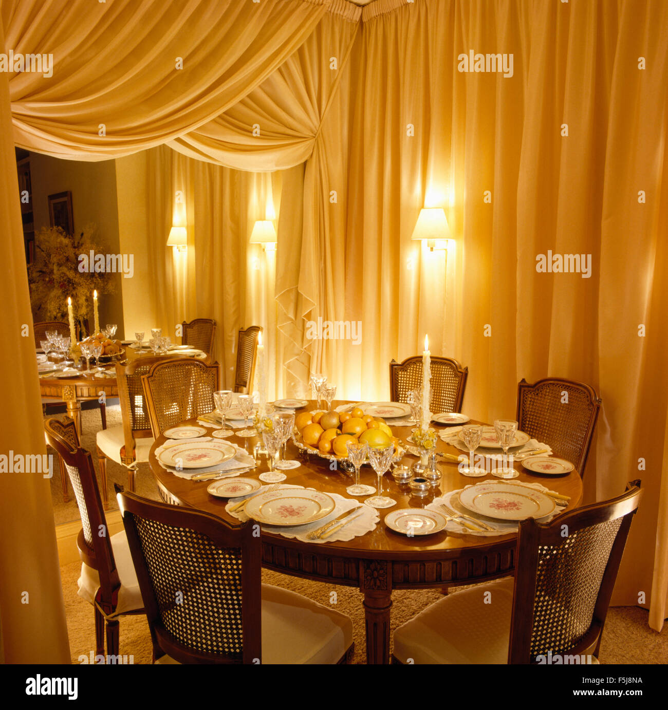 Drappeggi su parete specchiata negli ottanta sala da pranzo con le lampade accese sul tavolo per la cena Foto Stock