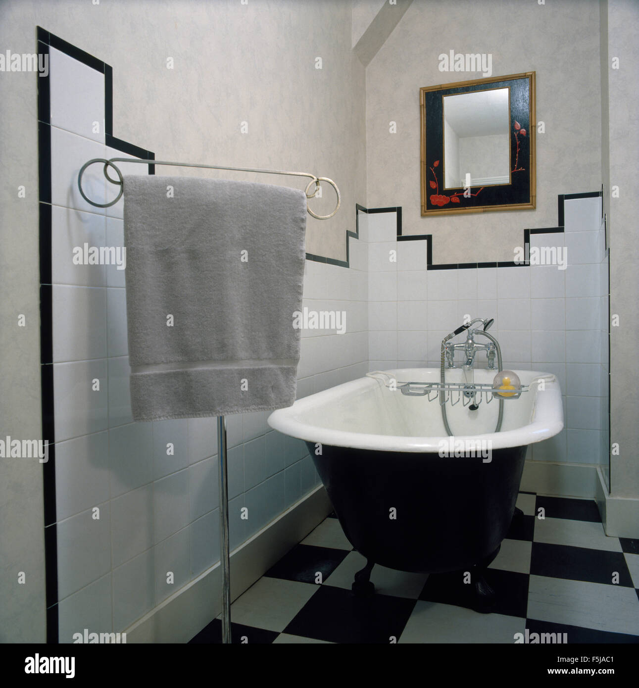 Roll-top bagno e nero+white chequerboard pavimento piastrellato in un bagno degli anni ottanta con un alto chrome asciugamano stand Foto Stock