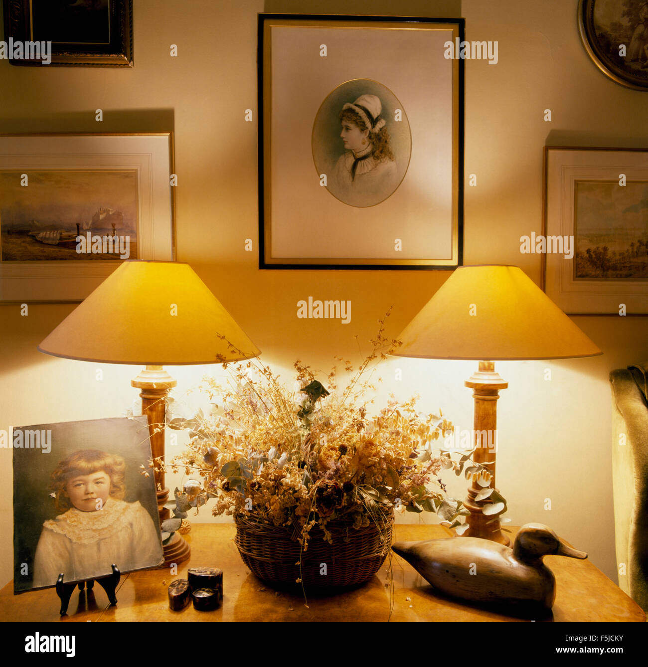 Le immagini sulla parete sopra le lampade illuminate su entrambi i lati di una ciotola di fiori secchi su un tavolo a lato in un ottanta sala da pranzo Foto Stock