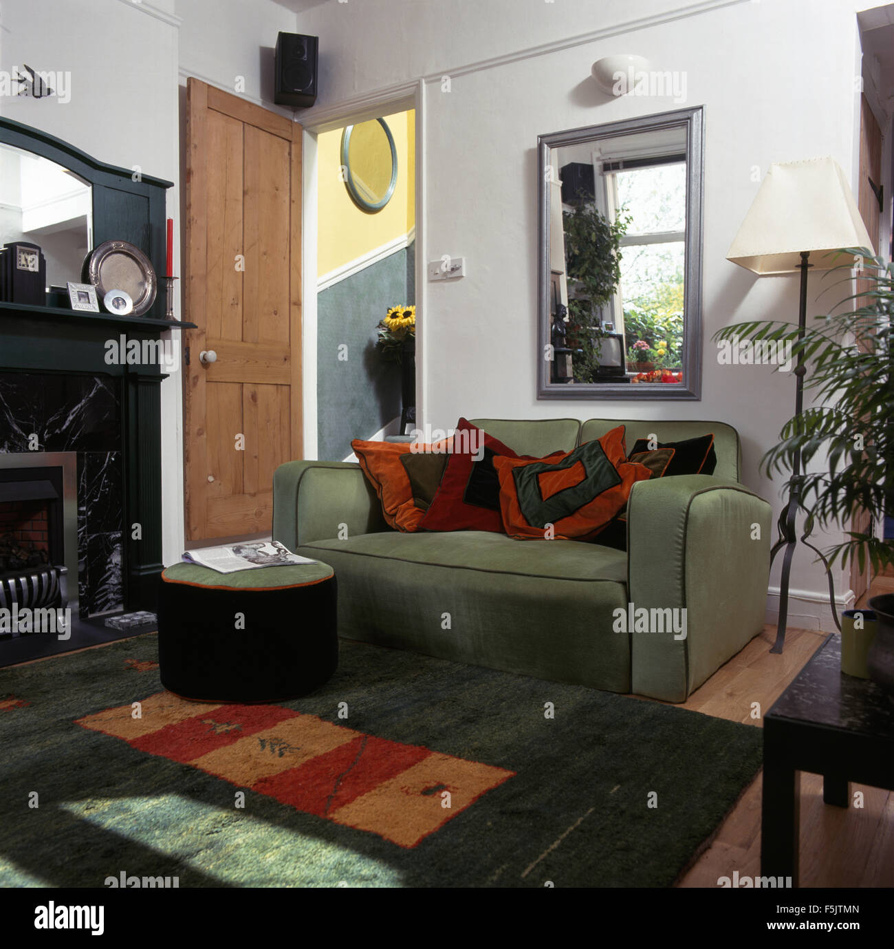 Green pouf e divano sotto una finestra interna in uno degli anni novanta soggiorno con una verde e arancione tappeto a motivi geometrici Foto Stock