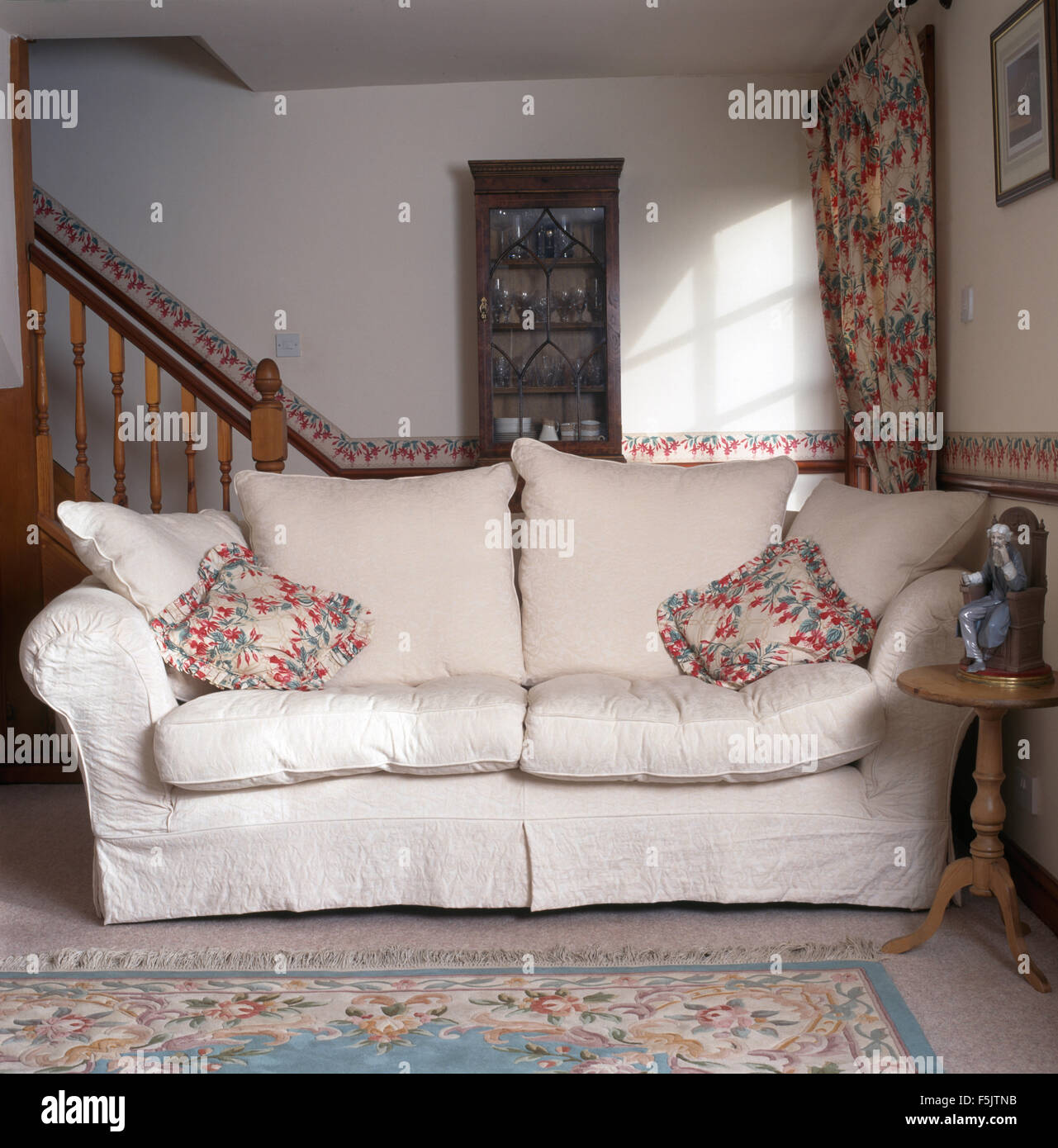 Cuscini floreali e bianco coperchio allentato su un divano in una piccola degli anni novanta soggiorno Foto Stock