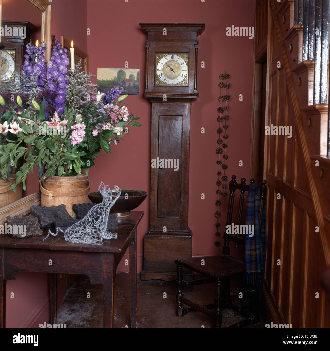 Estate floreali sul tavolo console in uno degli anni novanta cottage rosa sala con un antico lungo caso orologio e sedia in legno Foto Stock