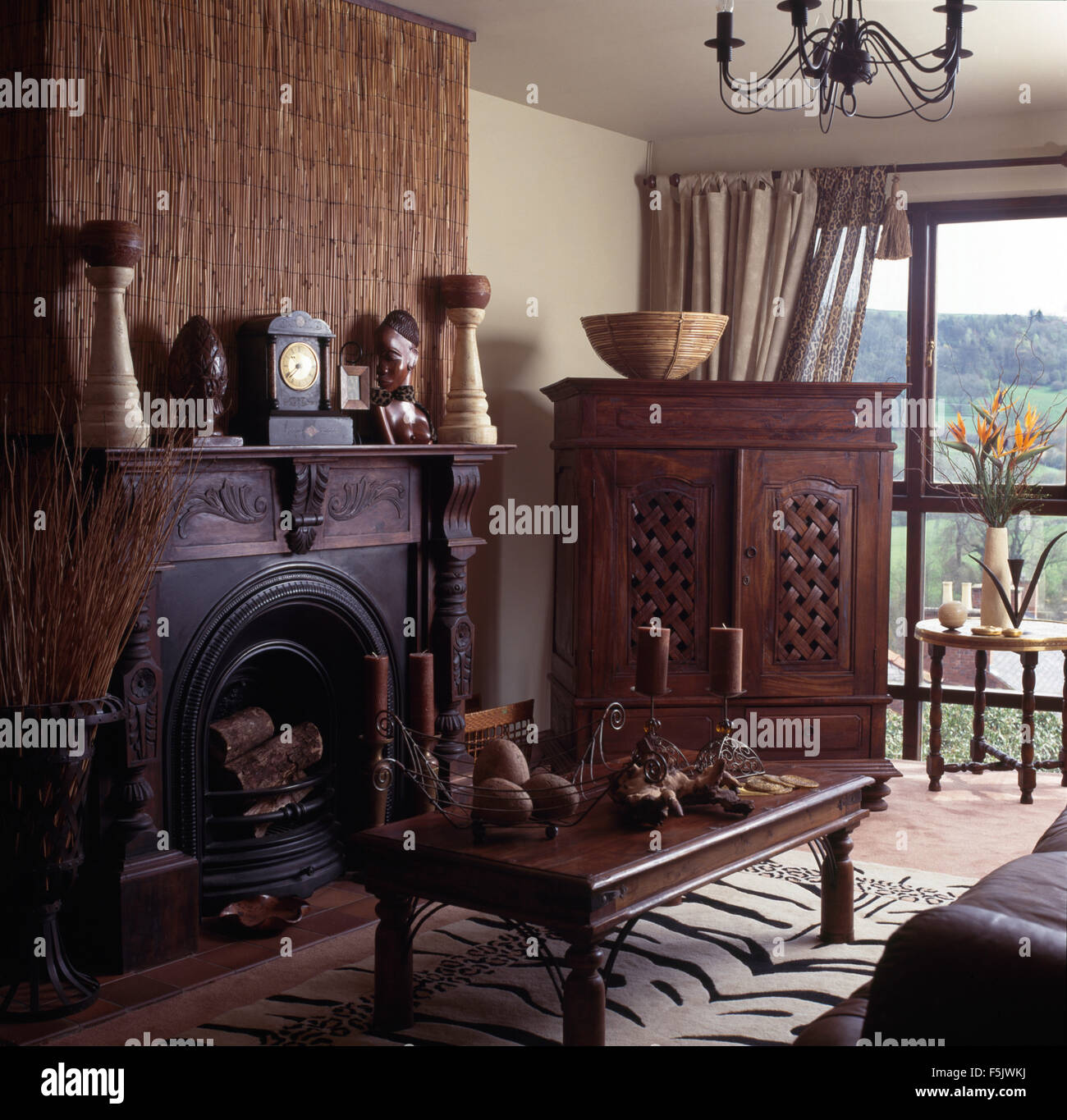 Pinoleum schermo sopra la ghisa caminetto in stile etnico degli anni novanta soggiorno con un armadio Indonesiano e tavolo da caffè Foto Stock