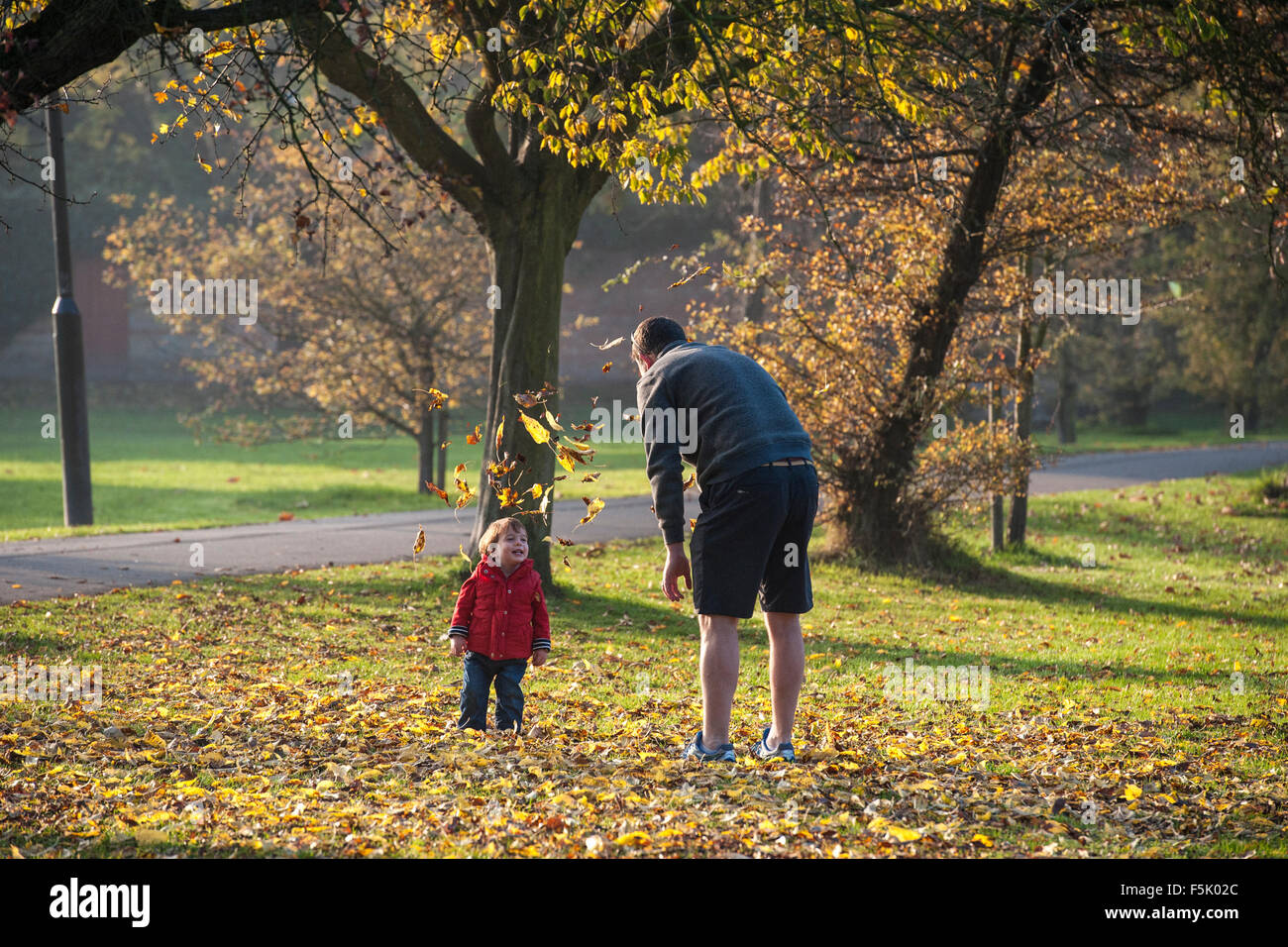 Un uomo getta caduta foglie in aria per il suo bambino in un parco di Londra Foto Stock