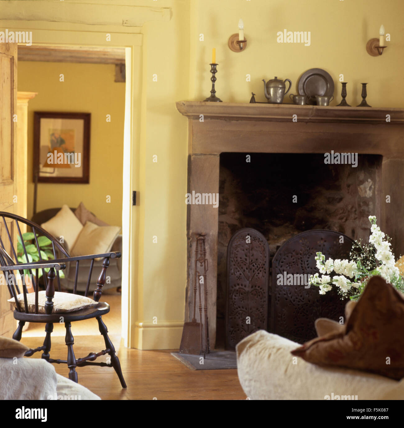Ferro battuto schermo fuoco nel camino in giallo pallido cottage soggiorno con un antico sedia Windsor Foto Stock