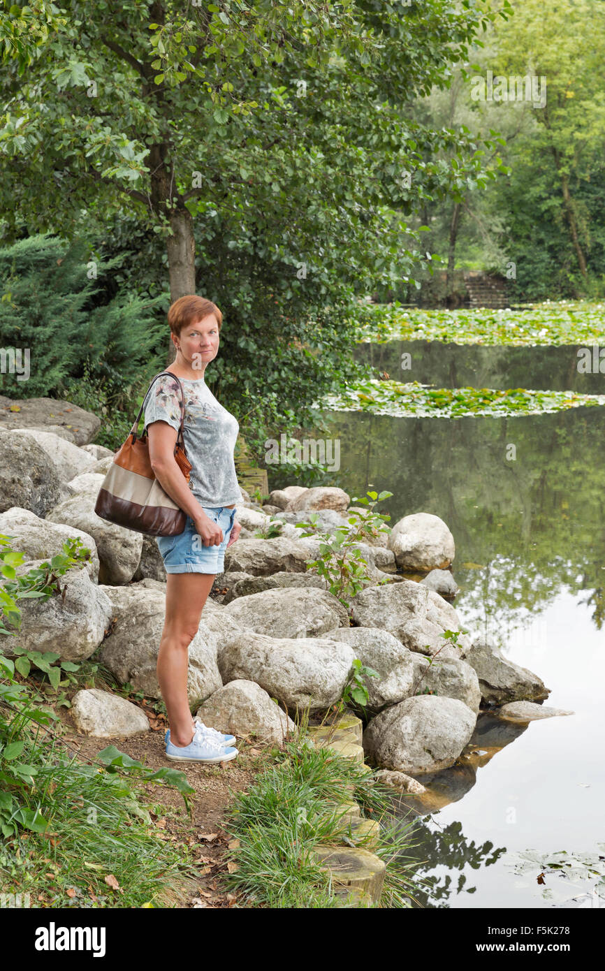Persone di mezza età abbronzata donna caucasica si erge sulle rive del pittoresco lago di Foto Stock