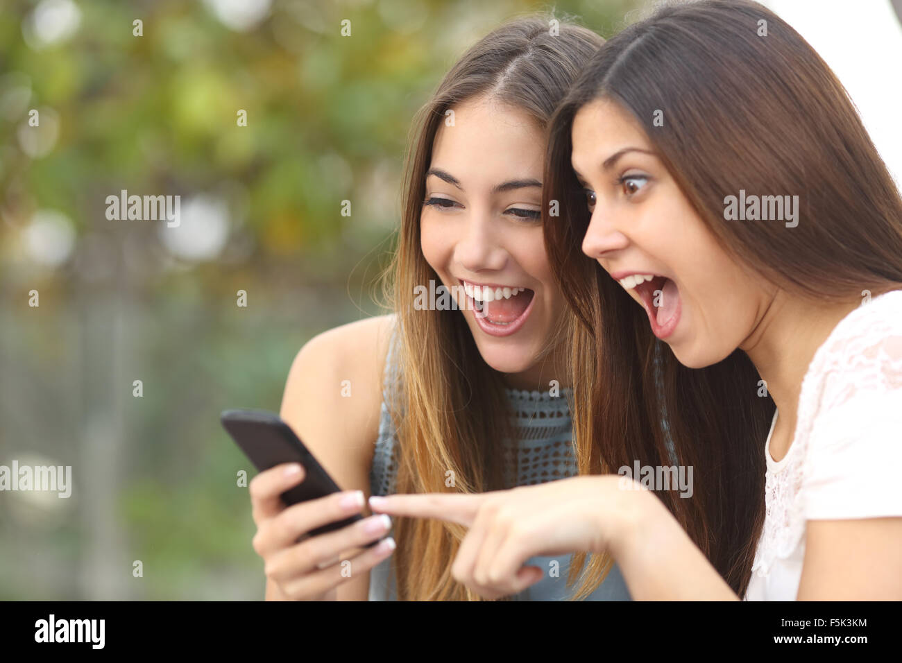 Euforico amici guardare i video su uno smartphone e che puntano a sorpresa dello schermo Foto Stock