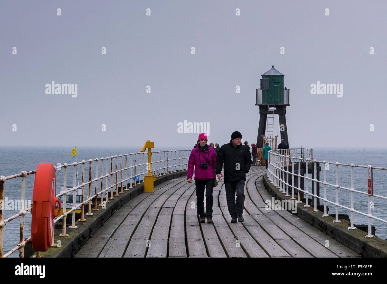 Persone in abiti caldi, camminando su Whitby West Pier estensione, England, Regno Unito - grigio di tavole di legno, il mare e il cielo, riflettono il vento freddo clima autunnale. Foto Stock