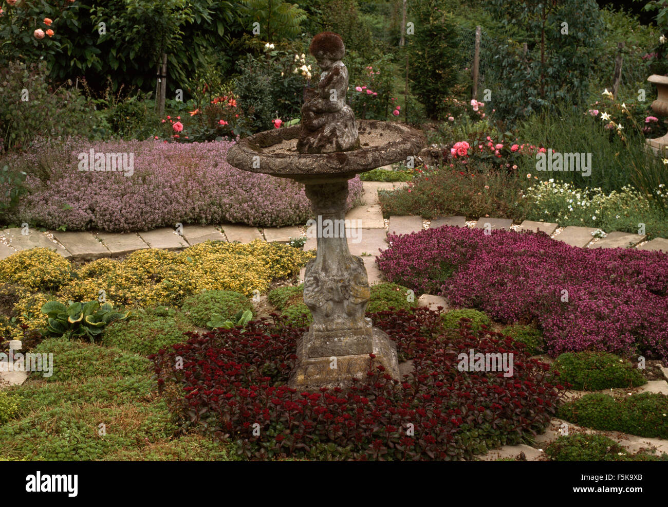 Antica pietra Bagno uccelli nel centro di un formale ruota di erbe nel paese grande giardino Foto Stock